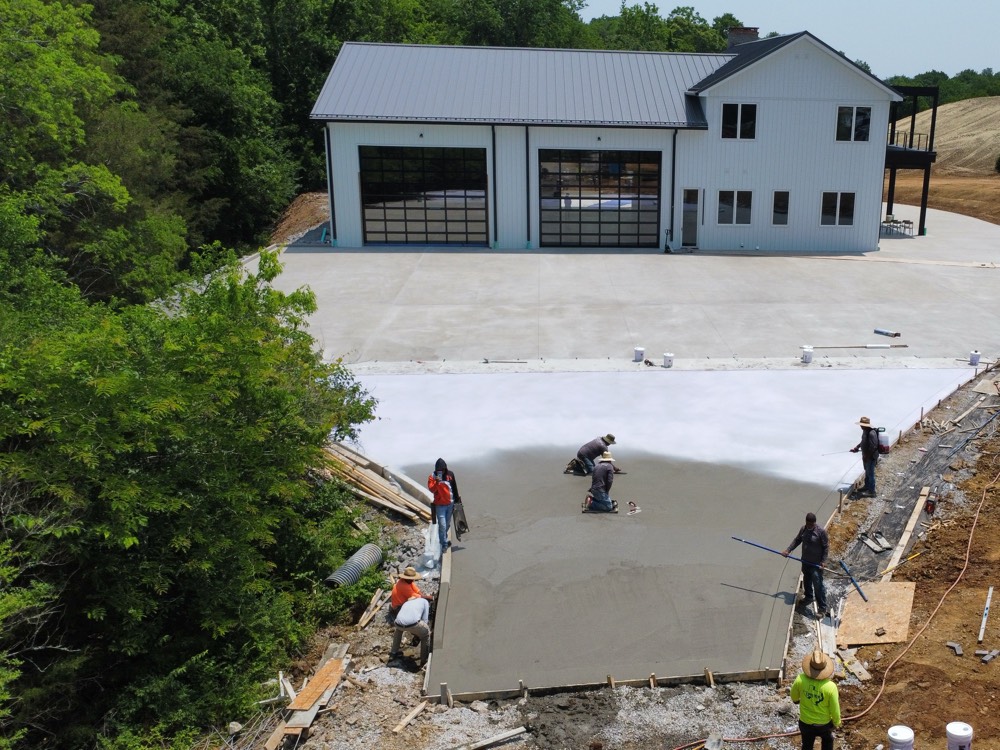 Aerial view of a new concrete drive and apron being placed at a Franklin barndominium, the crew finishing the fresh slab with topcast retarder applied across the poured section behind them