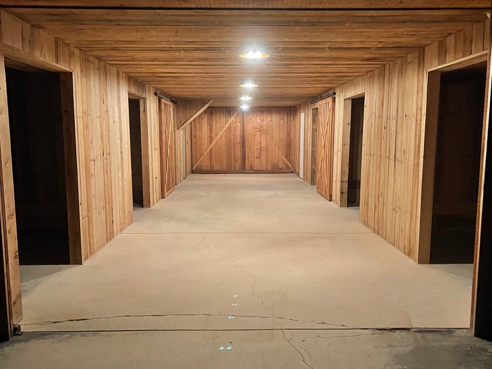 The same barn aisle before staining, bare gray concrete under new cedar stalls