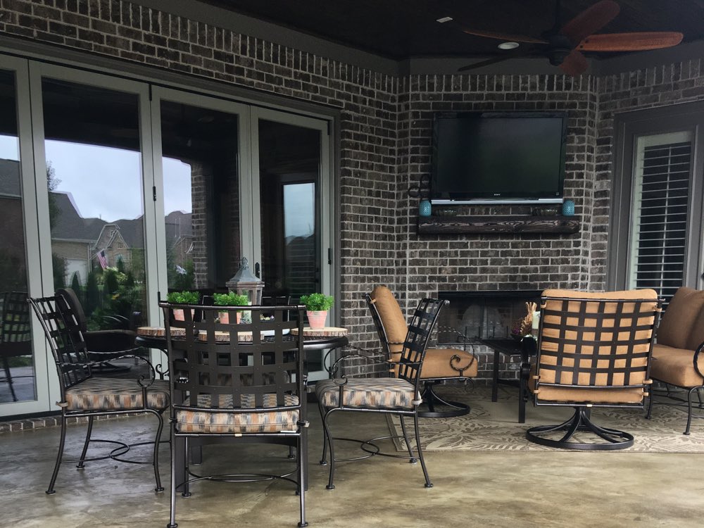Covered brick porch in Thompson's Station with an outdoor fireplace, the slab stained a warm mottled tan and furnished with a dining set