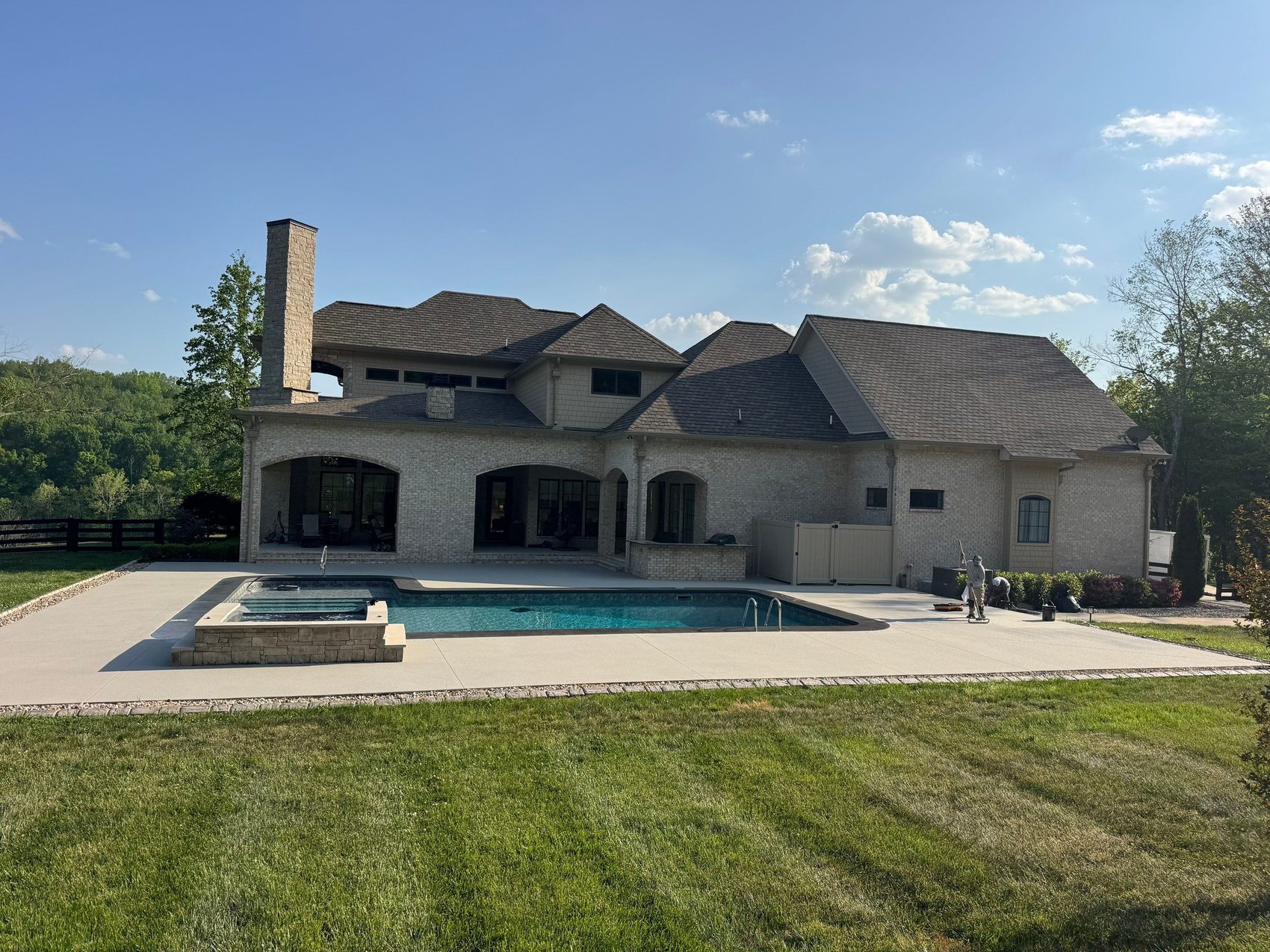 Estate pool deck and spa coping resurfaced in a durable architectural quartz finish behind a large brick home in Hendersonville